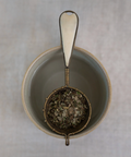 Tea strainer with tea leaves in a ceramic bowl on a textured surface