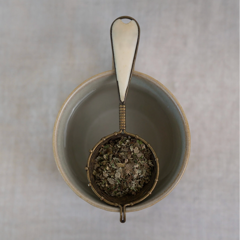 Tea strainer with tea leaves in a ceramic bowl on a textured surface