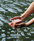 Hand holding a bar of soap over water with soap suds.