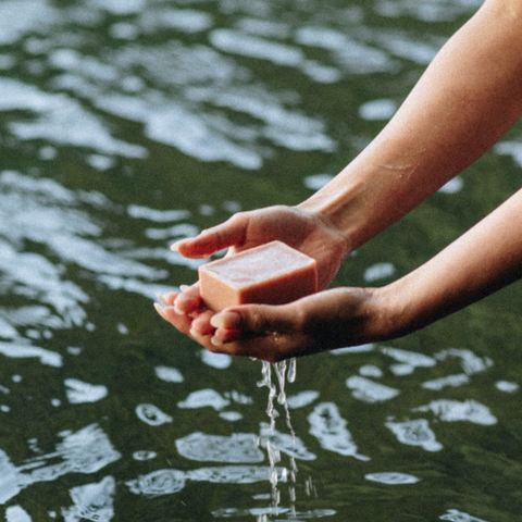 Hand holding a bar of soap over water with soap suds.