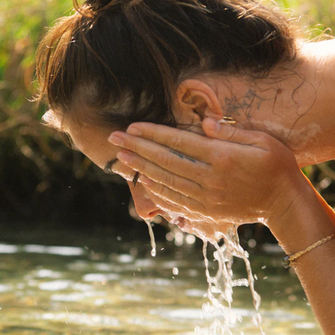 Person washing their face with water outdoors