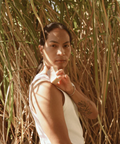Person standing among tall grass wearing a white sleeveless shirt and brown pants.