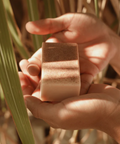 Hand holding a square bar of soap with grass in the background