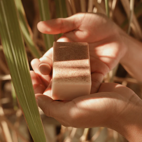 Hand holding a square bar of soap with grass in the background