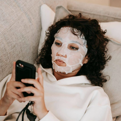 Woman with a face mask using a phone on a couch