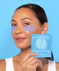 Woman wearing eye patches with a 'patchology' product packaging against a blue background