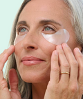 Woman applying eye patches to her face with a light blue background