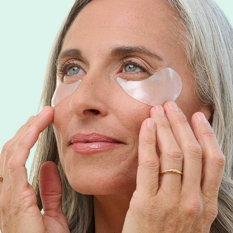 Woman applying eye patches to her face with a light blue background
