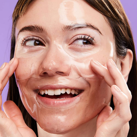 Woman applying a skincare product on her face with a purple background