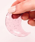 Hand holding a pink glittery crescent moon-shaped object against a white background