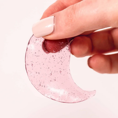Hand holding a pink glittery crescent moon-shaped object against a white background