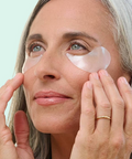 Woman applying pink eye patches to her eyes with a light blue background