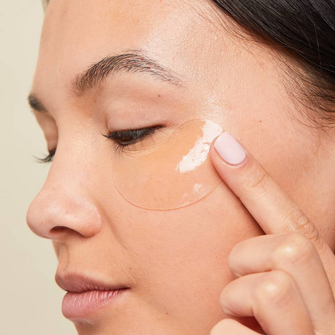 Person applying cream to their face with a neutral background