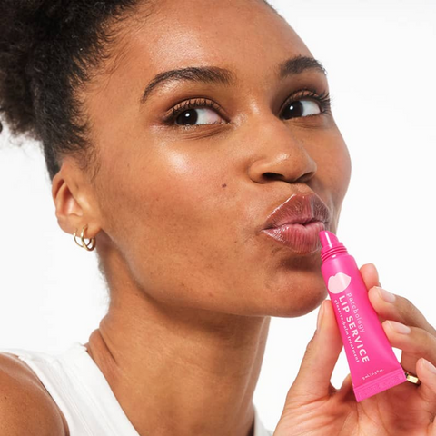 Woman applying pink lip balm labeled 'Lip Service' on a white background