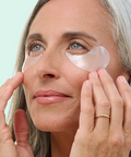 Woman applying pink eye patches to her eyes with a light blue background