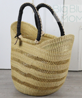 Woven straw bag with black handles on a wooden floor.