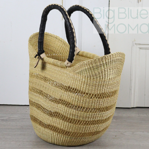 Woven straw bag with black handles on a wooden floor.