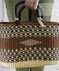 Woven basket with black and beige pattern held by a person wearing green pants.