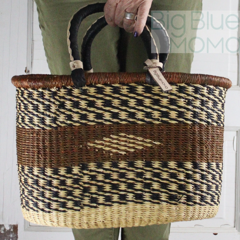 Woven basket with black and beige pattern held by a person wearing green pants.