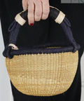Handbag with black handle and natural woven body held by a person.