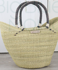 Woven straw tote bag with black handles on a light wooden floor.