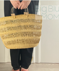 Person holding a woven basket with 'Big Blue Momo' branding in the background