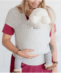 Woman wearing a baby in a white baby carrier against a plain background