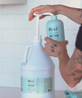 Person pouring Mint body wash from a smaller bottle into a larger container.
