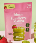 Pink package of blume Strawberry Matcha Superfood Latte Powder with strawberries and a green drink on a light green background.