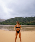 Woman in a black bikini standing on a beach with mountains in the background