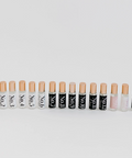 A row of small cosmetic tubes with beige caps and black-and-white labels, arranged horizontally on a light gray background. Small inset thumbnails appear along the left edge.