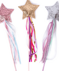 Three glittery star wand toppers in pink, gold, and silver, each with long multicolored ribbon tails, displayed on a white background.
