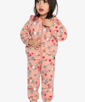 A young girl wearing a pink two-piece pajama set with a cartoon animal print, standing against a light gray background.