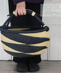 Person holding a black and beige woven basket against a white wall.