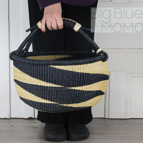 Person holding a black and beige woven basket against a white wall.