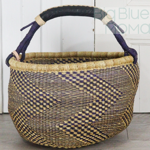 Woven basket with a checkered pattern and purple handles on a light wooden floor.