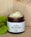 A jar of Sensitive Skin Nourisher moisturizer with a label that reads 'Sensitivity Skin Nourisher - Whipped Tattoo Cream', displayed on a wooden surface with a green moss decoration to the left.