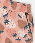 Close-up of a pair of children's pants featuring a pink background with a strawberry print in shades of brown, cream, and blue.