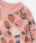 A close-up of a children's long-sleeve top featuring a pink strawberry print. The design includes strawberries in shades of brown, dusty rose, and cream, with dark teal-green leafy tops.