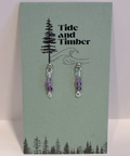 Pair of purple beaded earrings on a Tide and Timber branded card with tree and wave design.