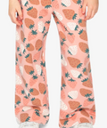 A person wearing wide-leg pink pants with a strawberry print, paired with a pink long-sleeve top and white sneakers, shown from the waist down on a light gray studio background.
