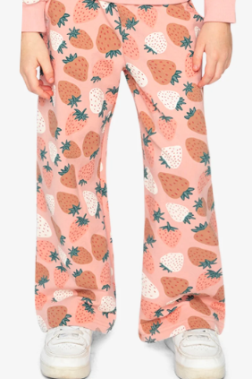 A person wearing wide-leg pink pants with a strawberry print, paired with a pink long-sleeve top and white sneakers, shown from the waist down on a light gray studio background.