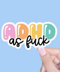 Colorful 'ADHD as fuck' sticker held by a hand against a light blue background