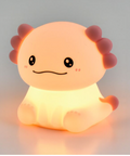 A cute, cartoonish axolotl-shaped night light glowing with a warm yellow and orange light, set against a soft gray background.