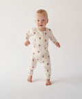 Baby standing on a white background wearing a white onesie with small patterns.