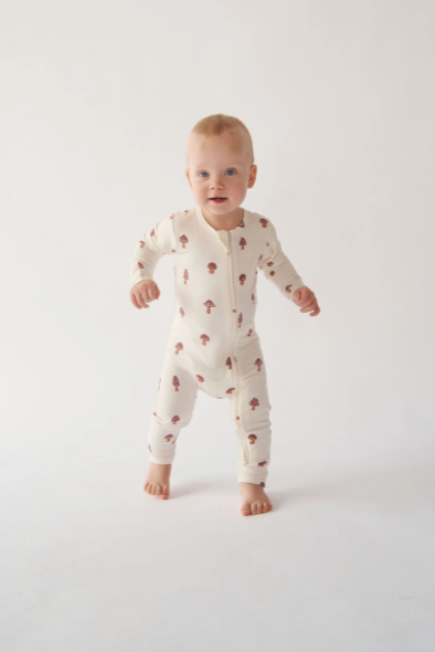 Baby standing on a white background wearing a white onesie with small patterns.