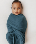 Newborn baby wrapped in a teal swaddle on a white background