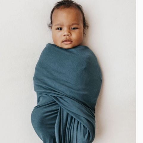 Newborn baby wrapped in a teal swaddle on a white background