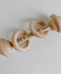Wooden baby rattle with 'Kaks & Valleys Baby' branding on a light gray background