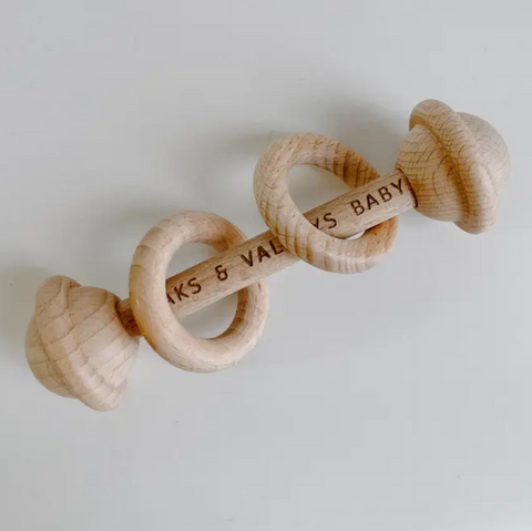 Wooden baby rattle with 'Kaks & Valleys Baby' branding on a light gray background